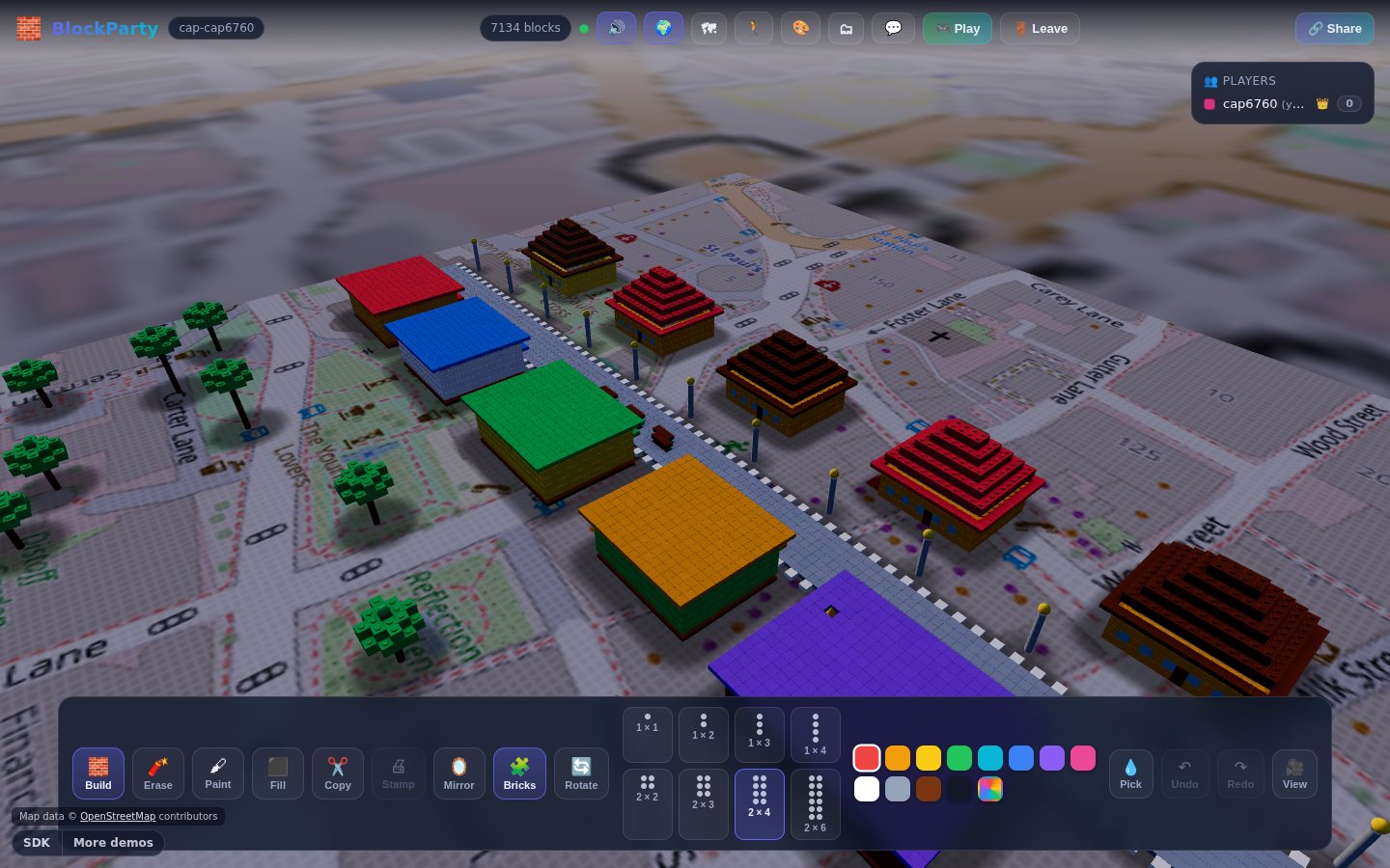 A voxel old town standing on the real streets by St Paul's, with the OpenStreetMap ground painted under the blocks and the build toolbar along the bottom.